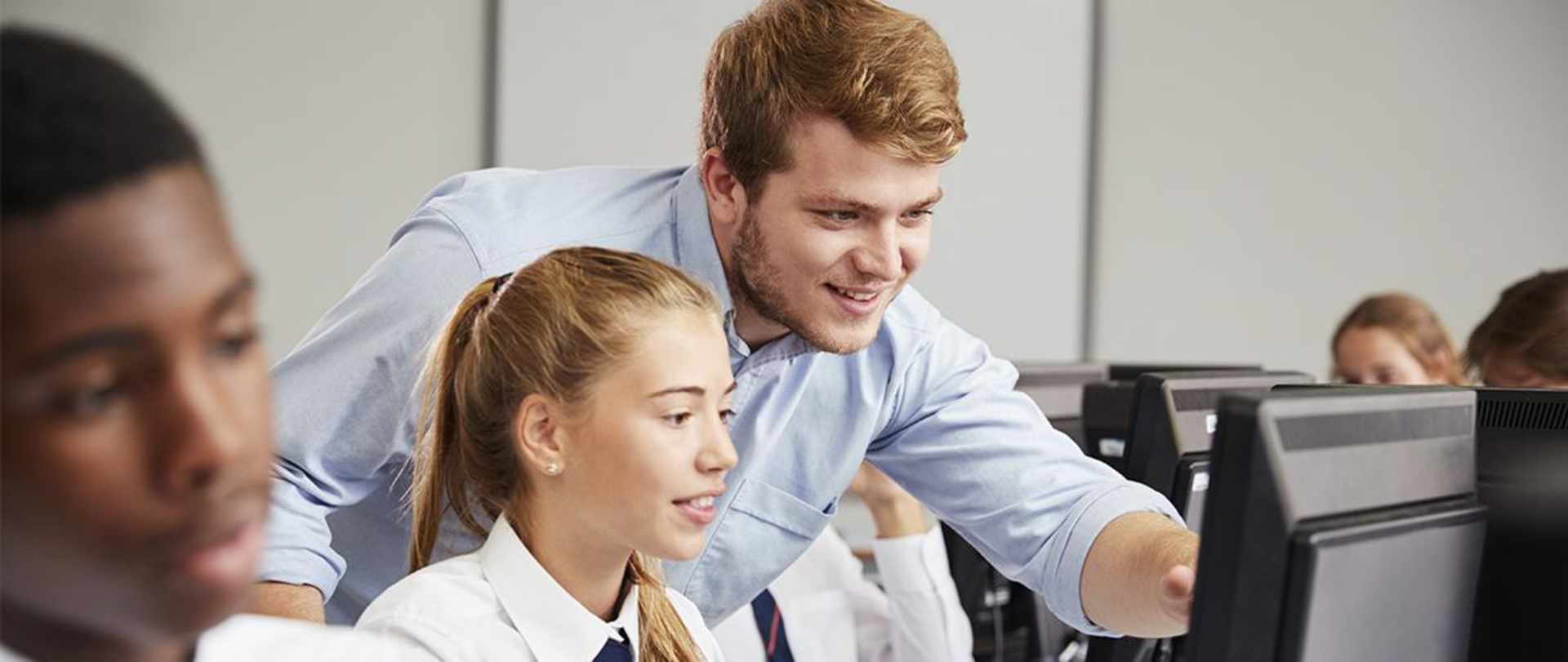 A secondary school teacher pointing to something on a pupil’s computer screen.