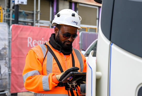 An image of a person entering details into a digital device on a construction site