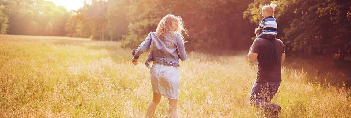 A family walks through a field as part of a walking route in Oxted. A child sits on the shoulders of one of the parents, smiling at the other parent who walks alongside them.