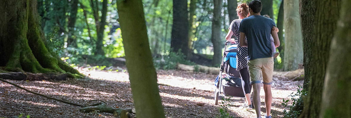 A family walking through a woodland, as part of an Oxted walk. One parent pushes a buggy, while the other parent carries a child in their arms.