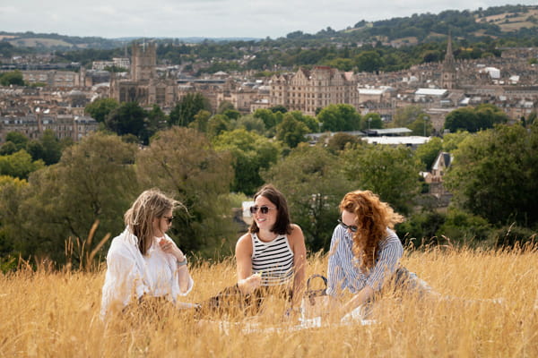 Three females sitting down in tall, wheat grass chatting and laughing