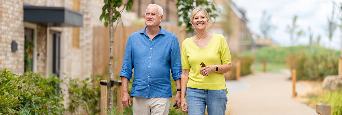 Julia and Michael walking along a newly paved and landscaped pedestrian path alongside new build homes.