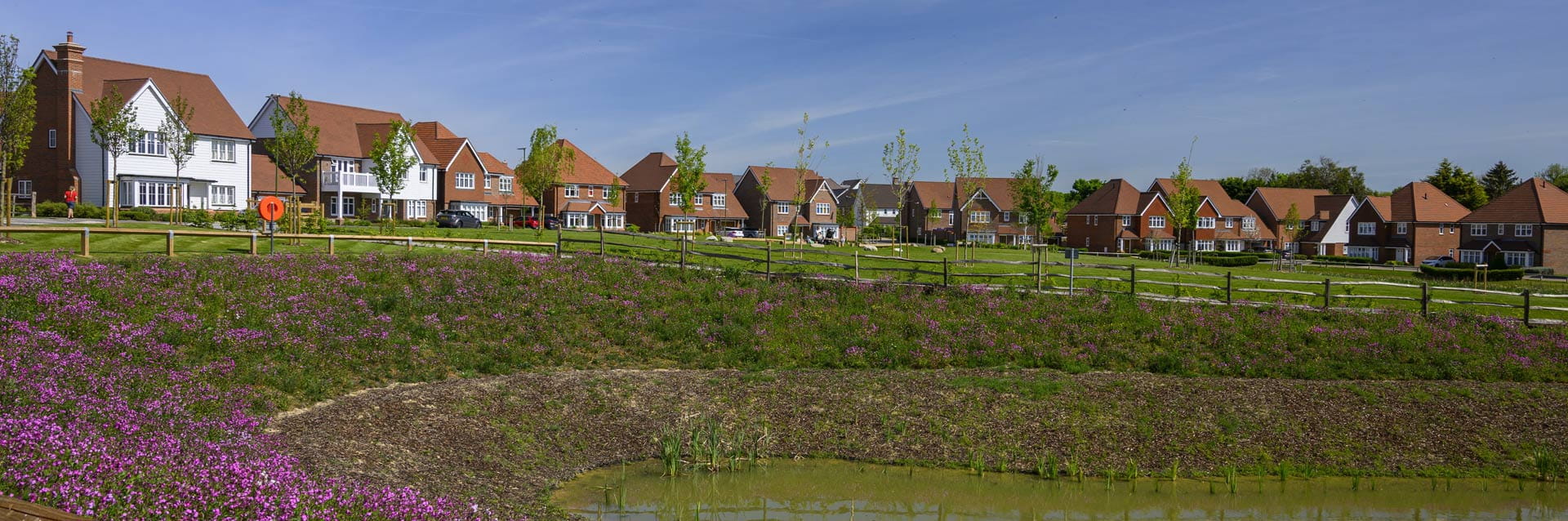 A row of houses with a pond and grassy slope in front of them