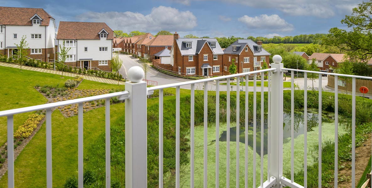A view of Hollyfields development from the balcony of a new build apartment, including a pond and green spaces overlooked by other homes.