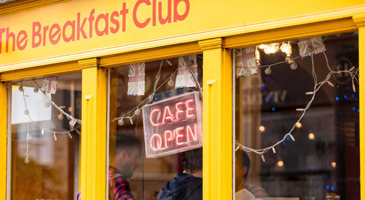 The exterior of The Breakfast Club cafe. The building has a retro appearance and features a bright yellow shopfront with orange writing.
