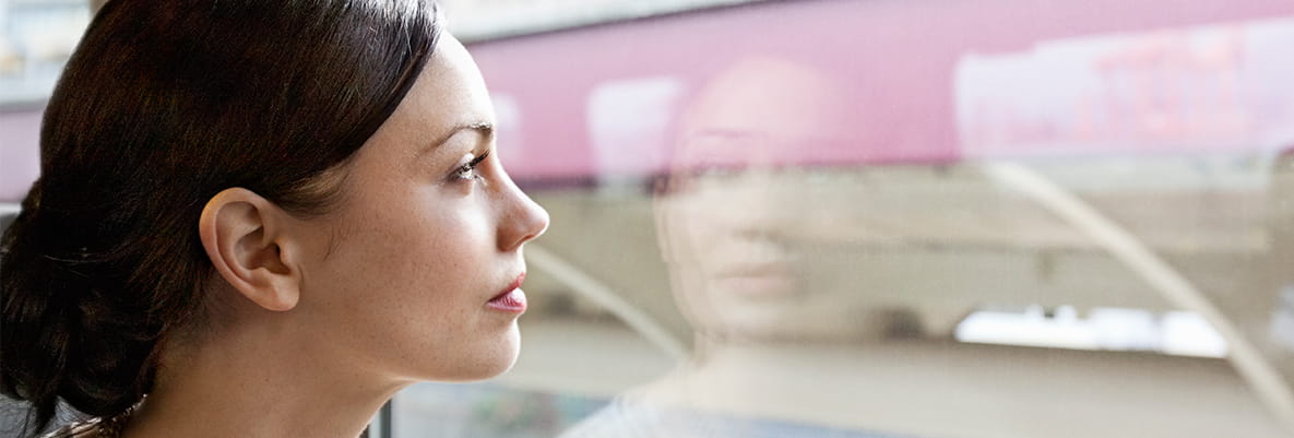 A commuter sitting on a train, looking out of the window as they travel to their destination. 