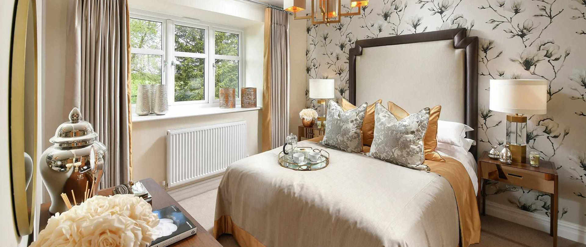 A large, luxurious bedroom in Berkeley Group’s Princes Chase development. Behind the large bed frame is a floral wallpaper, featuring a black and white floral print.