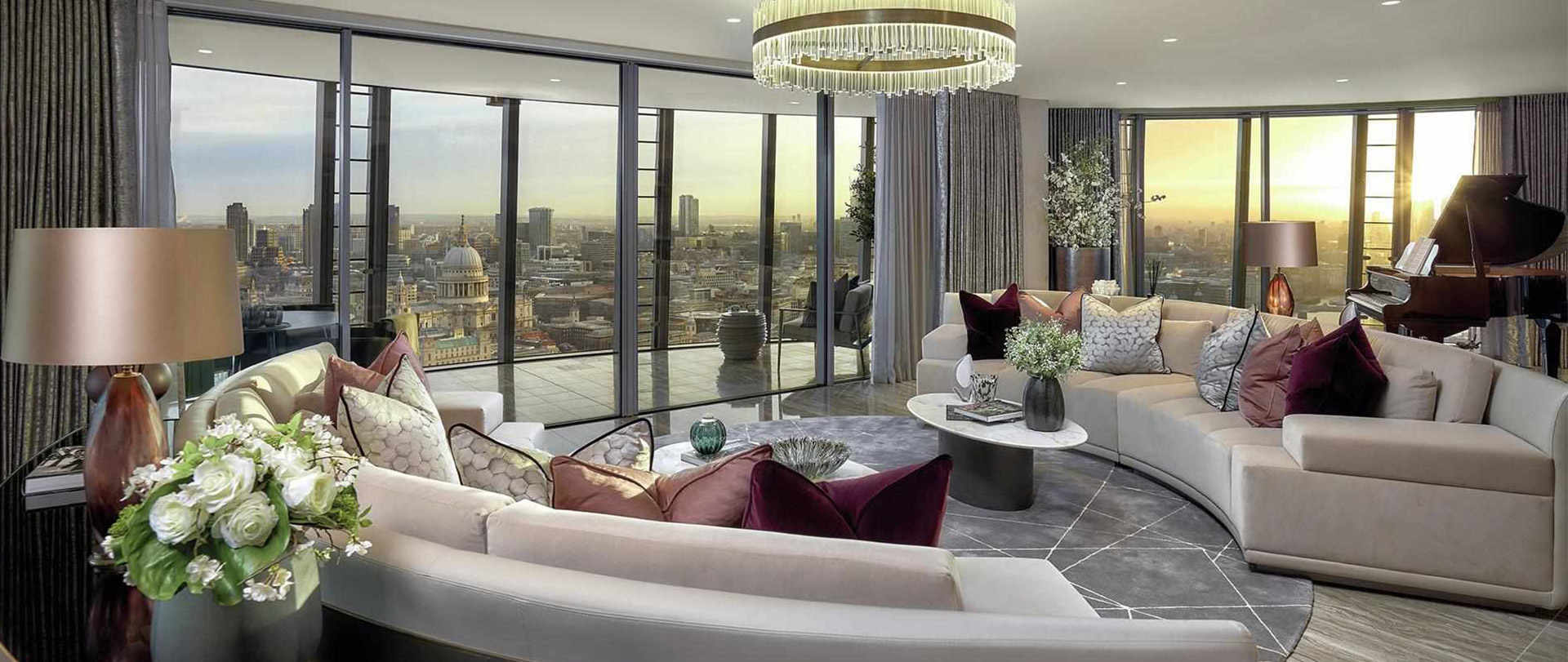 A spacious, modern living room in One Blackfriars, a Berkeley Group development. The room features a curved sofa, a grand piano, and a large chandelier.