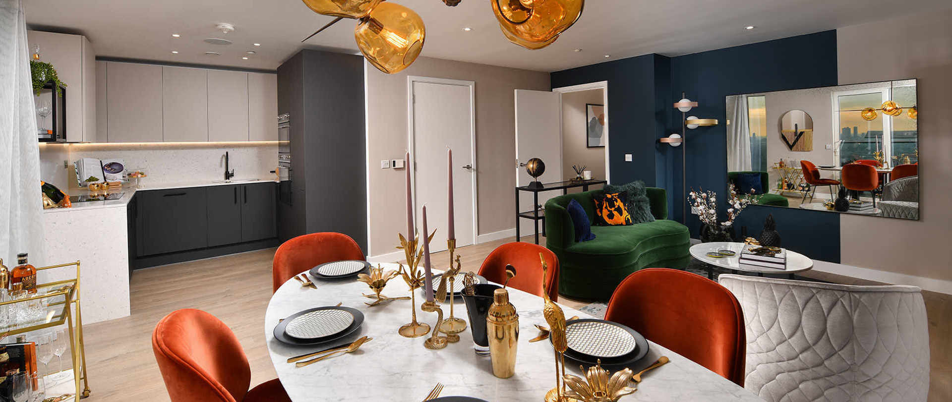 A large, open-plan apartment with a stylish dining and living area. The space features red velvet chairs at the dining table and a green velvet sofa in the background.