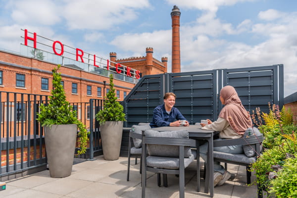 CGI of two people at a table on rooftop terrace with sign Horlicks on the building behind