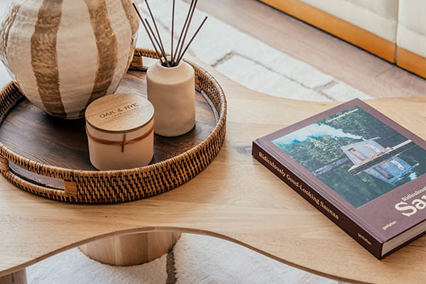 Closeup photo of wooden curved coffee table, with scented candles, vase and book as decorations
