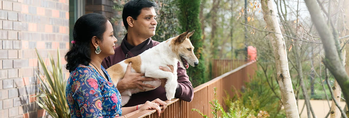 An image of the couple standing on the balcony of their apartment with their dog