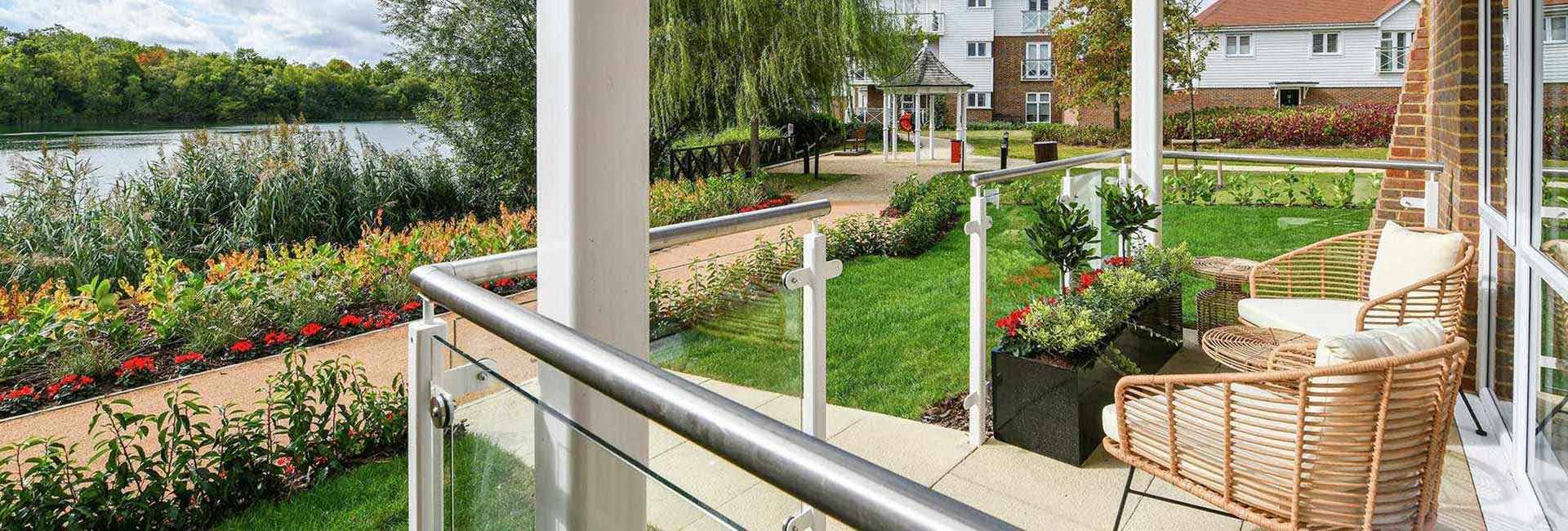 A balcony with wicker chairs overlooking a large pond and gardens.