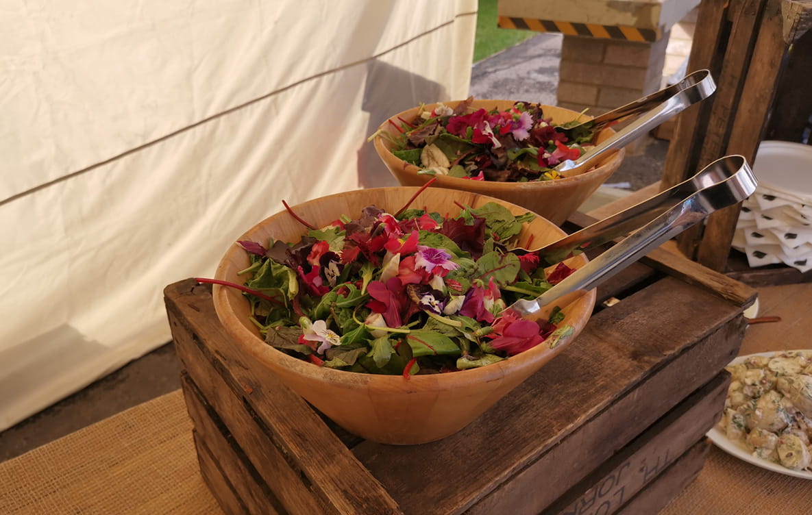 Two salad bowls on the side with serving tongs at a barbecue.