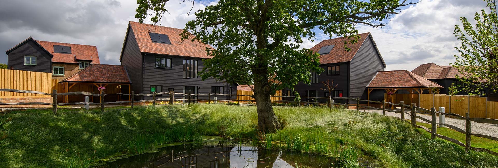 New build homes surrounded by greenery and a small pond in the foreground.