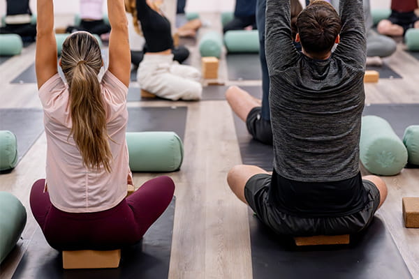 a pilates class in progress, male and female sitting cross-legged on mats stretching.