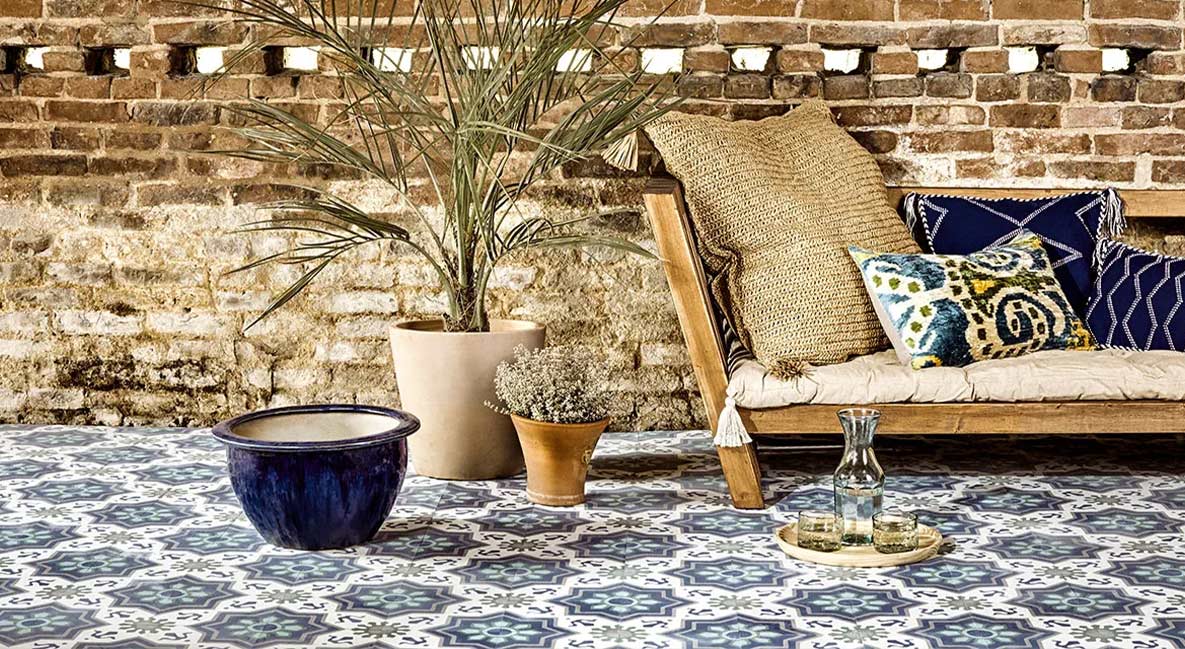 An outdoor seating area with colourful patterned tiles, a sofa and patterned cushions.