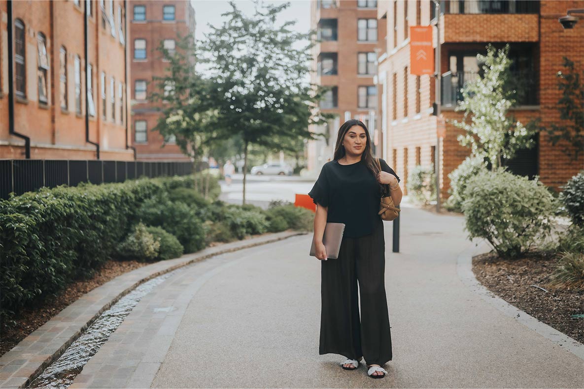 Faiza posing along a pedestrian path with new build flats either side.