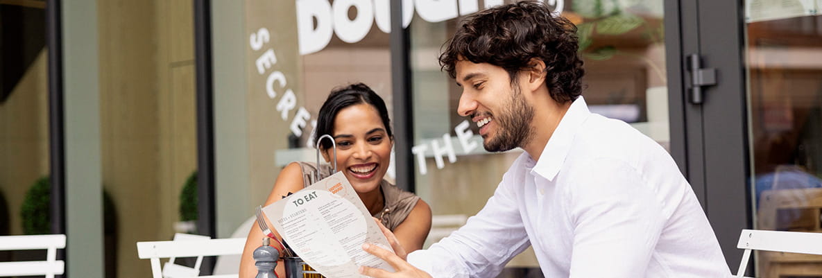 An image of a couple sat down at a cafe ordering from the menu