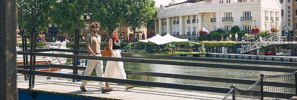 An image of a couple walking together on a bridge over the water