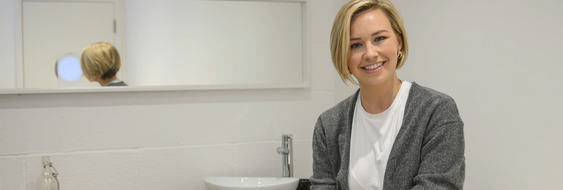 Lorna standing in the bathroom of her new home, smiling at the camera.