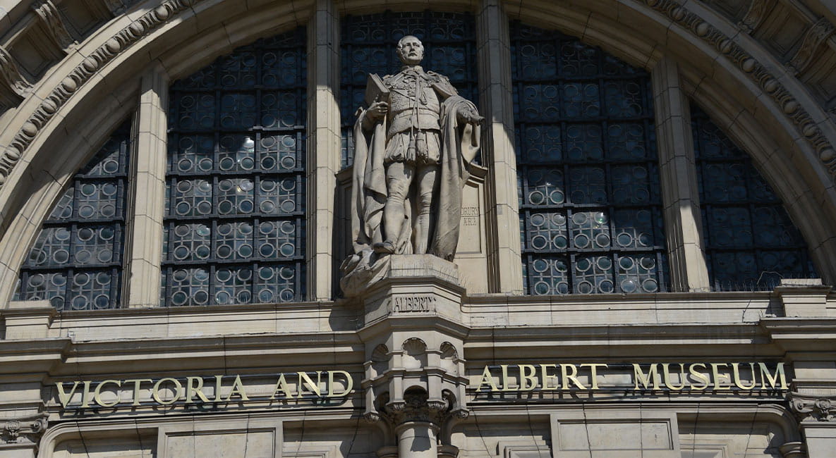 The exterior of the V&A museum, featuring a statue and a sign that reads ‘Victoria and Albert Museum’.