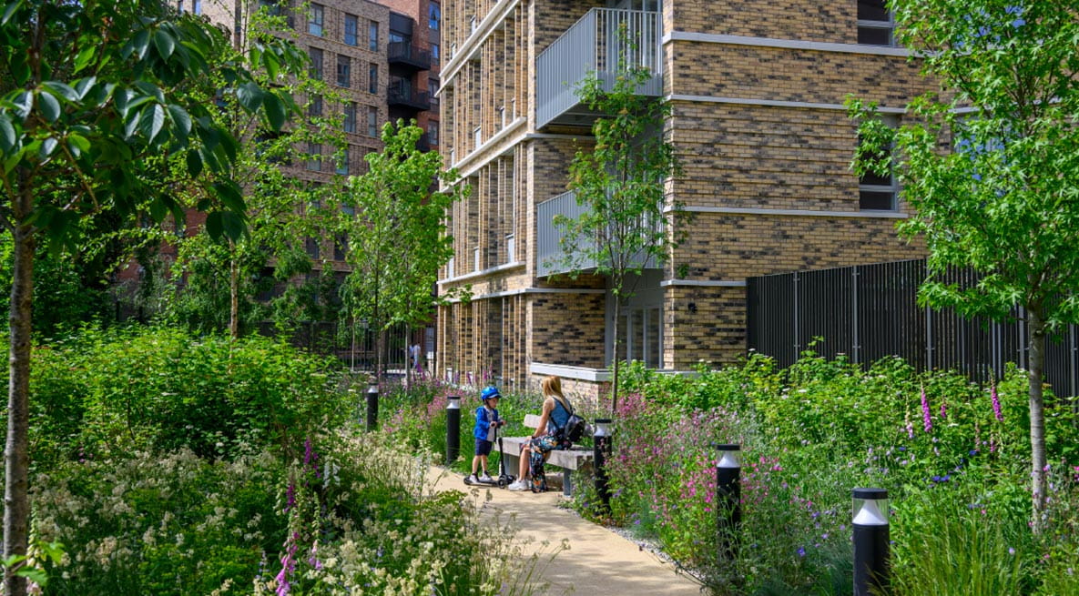 A mother and child are sitting by a bench within the landscaped gardens in Alexandra Gate