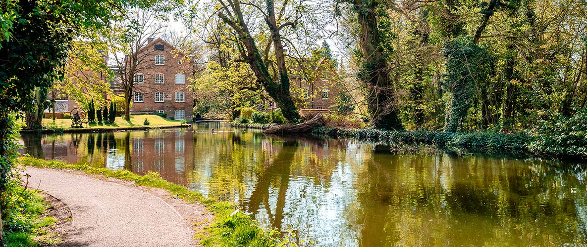 A public walkway running along a picturesque pond in a leafy Hertfordshire neighbourhood.