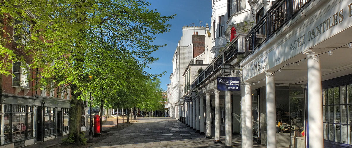 The charming high street of a picturesque Kent town, featuring rows of shops, trees and a red postbox among characterful period buildings.
