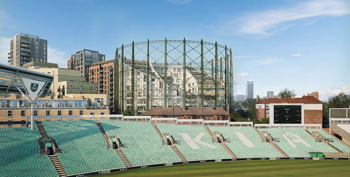 A cricket ground with green seating, a scoreboard, and a backdrop of buildings and a historic gasholder structure on a sunny day.