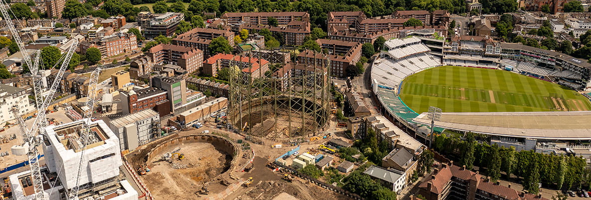 A panoramic view of an urban landscape featuring a stadium, residential buildings, green spaces, and an ongoing construction site.