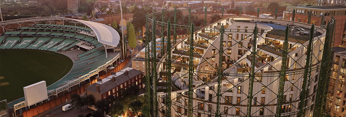 A scenic view of a cricket stadium to the left and a modern building with a circular framework to the right during sunset/rise.