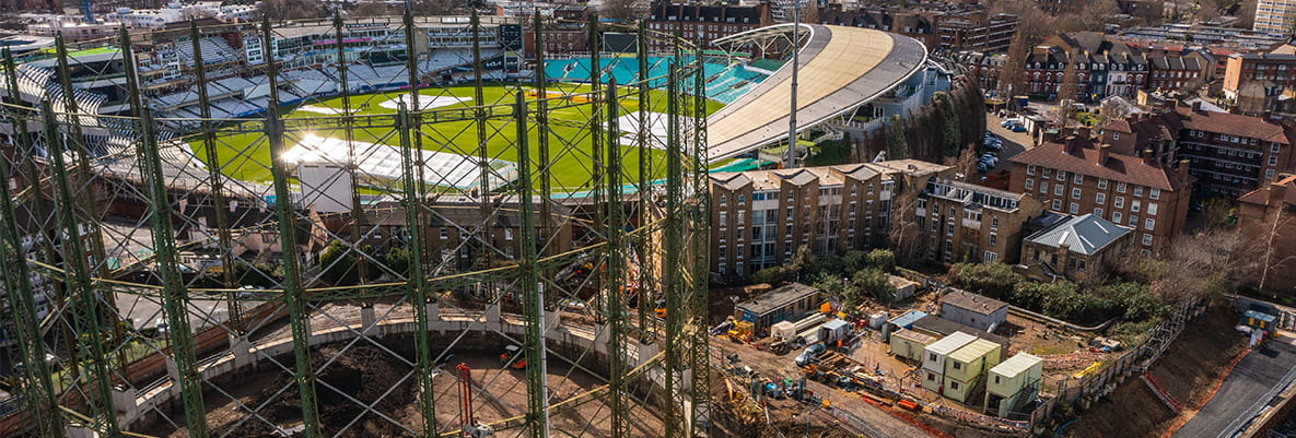 Aerial view of a sports stadium surrounded by urban buildings, including construction work with scaffolding and equipment nearby.