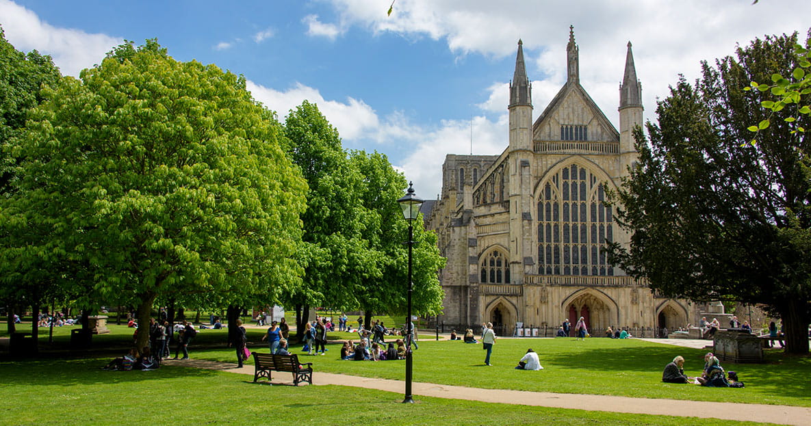 The exterior of Winchester Cathedral and its grounds on a sunny day.