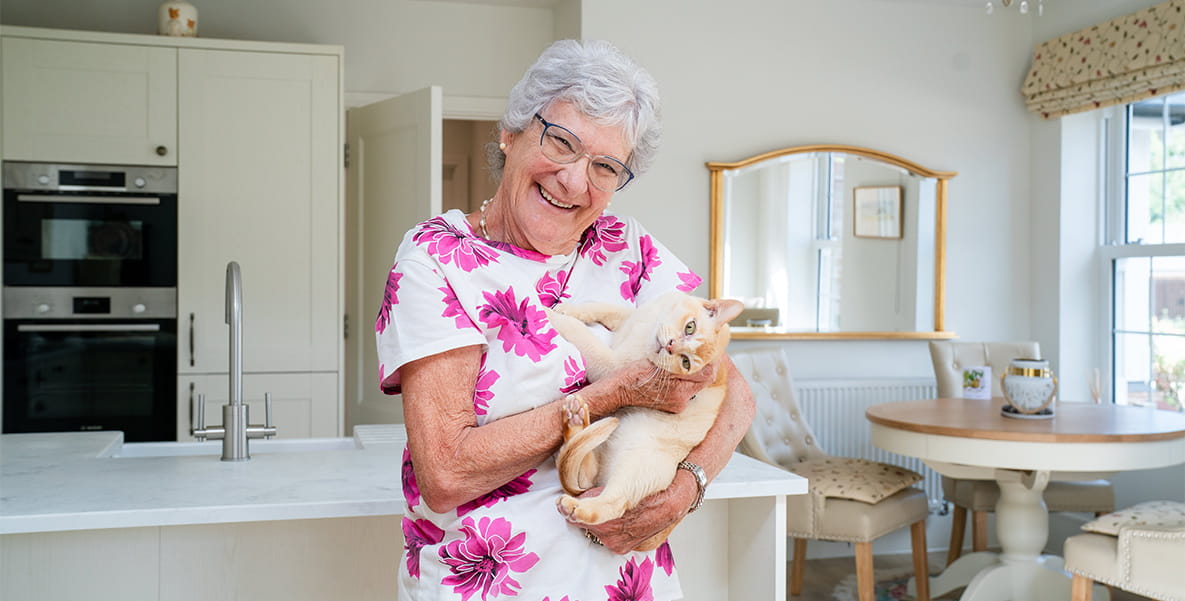 Elizabeth with her cat inside new build home interior kitchen dining space decorated in neutral tones.