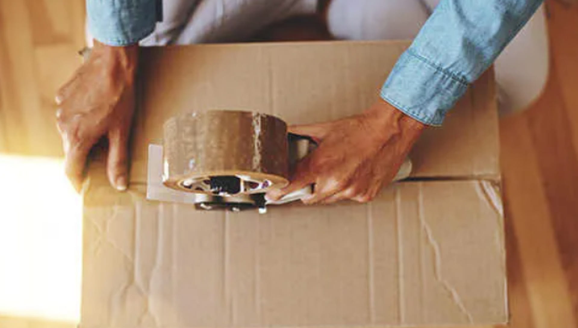A person sealing a cardboard box using parcel tape.
