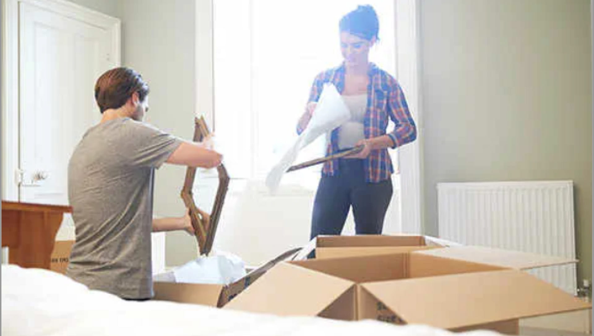 Two people packaging mirrors and photo frames into cardboard boxes.