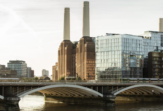Battersea Power Station with its four chimneys, seen across the River Thames with a bridge in the foreground