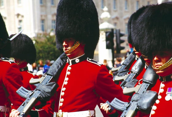 Royal Guards in red ceremonial uniforms and bearskin hats marching in formation