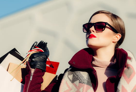 A woman wearing sunglasses and a scarf carrying shopping bags