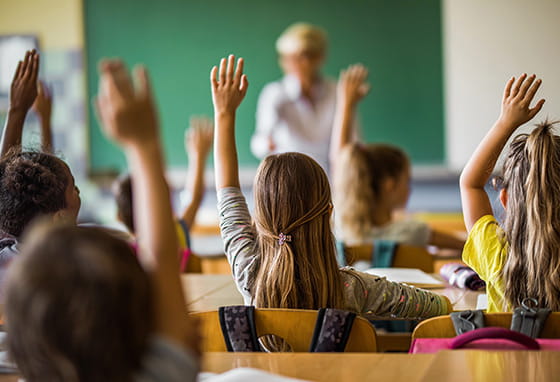 A group of children raising their hands in a classroom