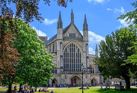 Winchester Cathedral in Hampshire, with people sitting on the grass in front