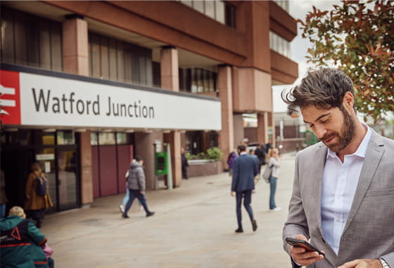Man in a suit looking at his phone outside Watford Junction train station