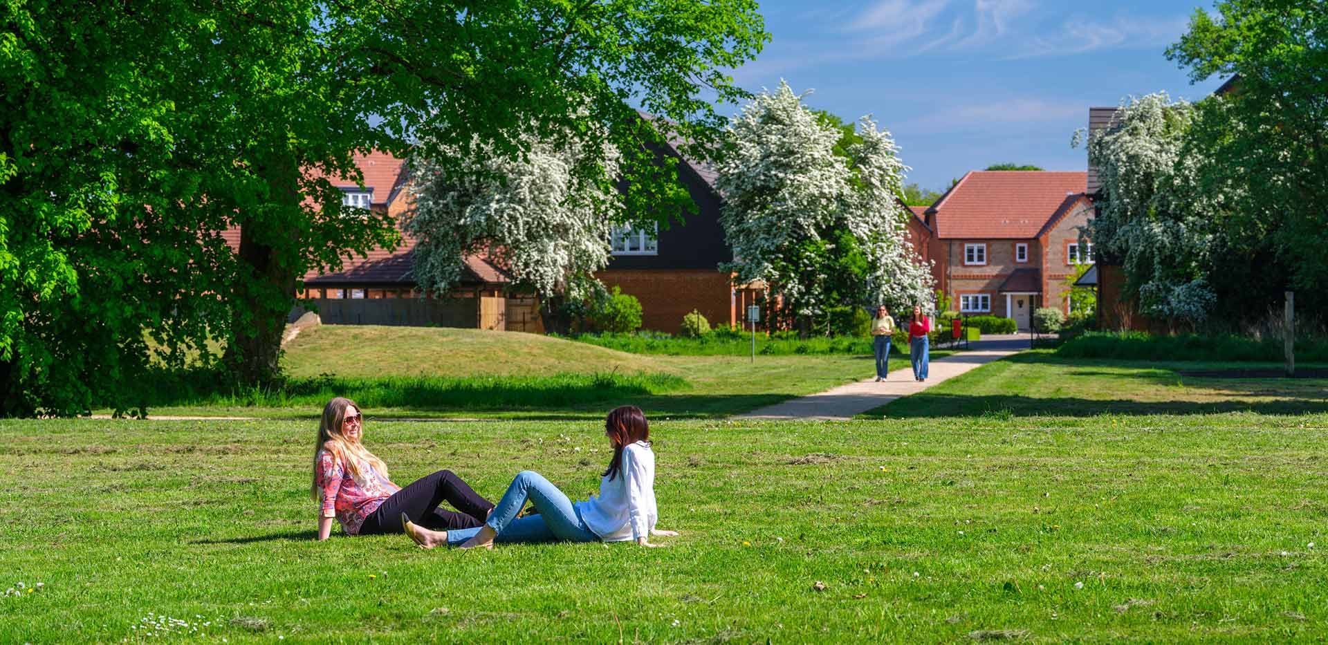An exterior image of The Ride at Abbey Barn Park with people sat on the field