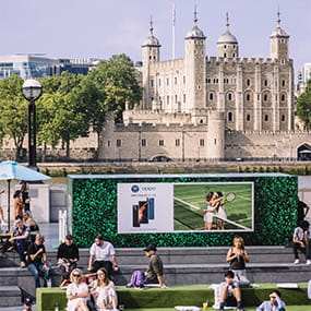 People reclining on artificial grass turf bleachers with historic landmark in the background