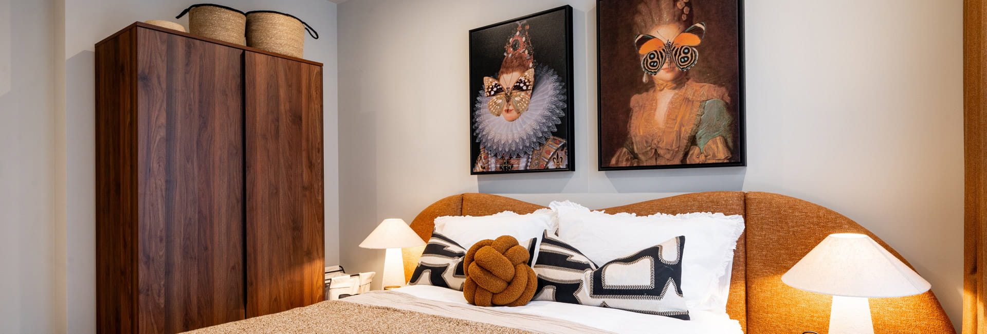 Closeup photo of double bed, tan-yellow headboard, wooden wardrobe, wall hangings