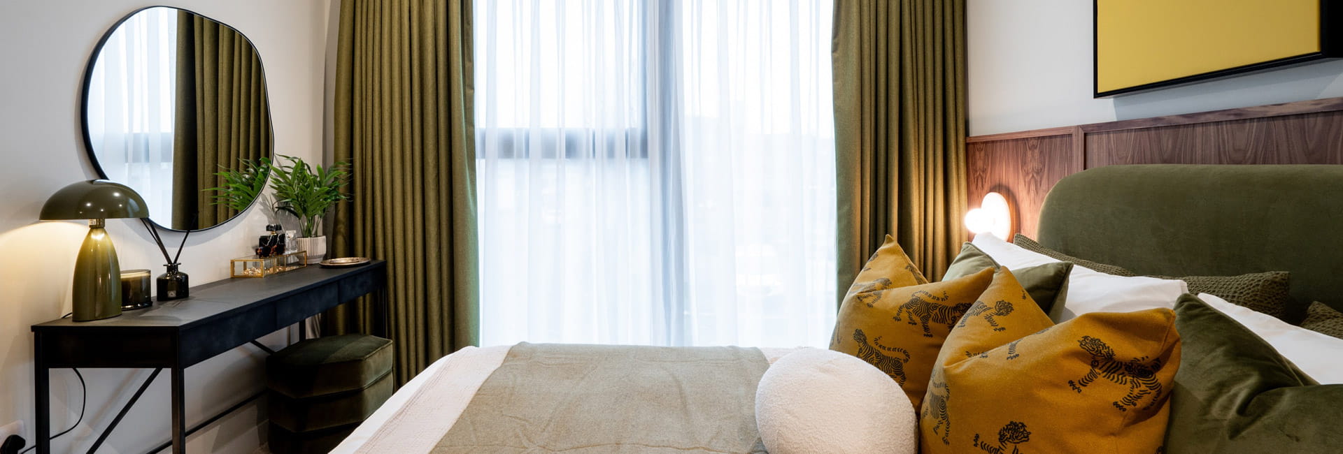 Closeup photo of double bed and window with curtains, moss-green design palette, vanity table with wall mirror