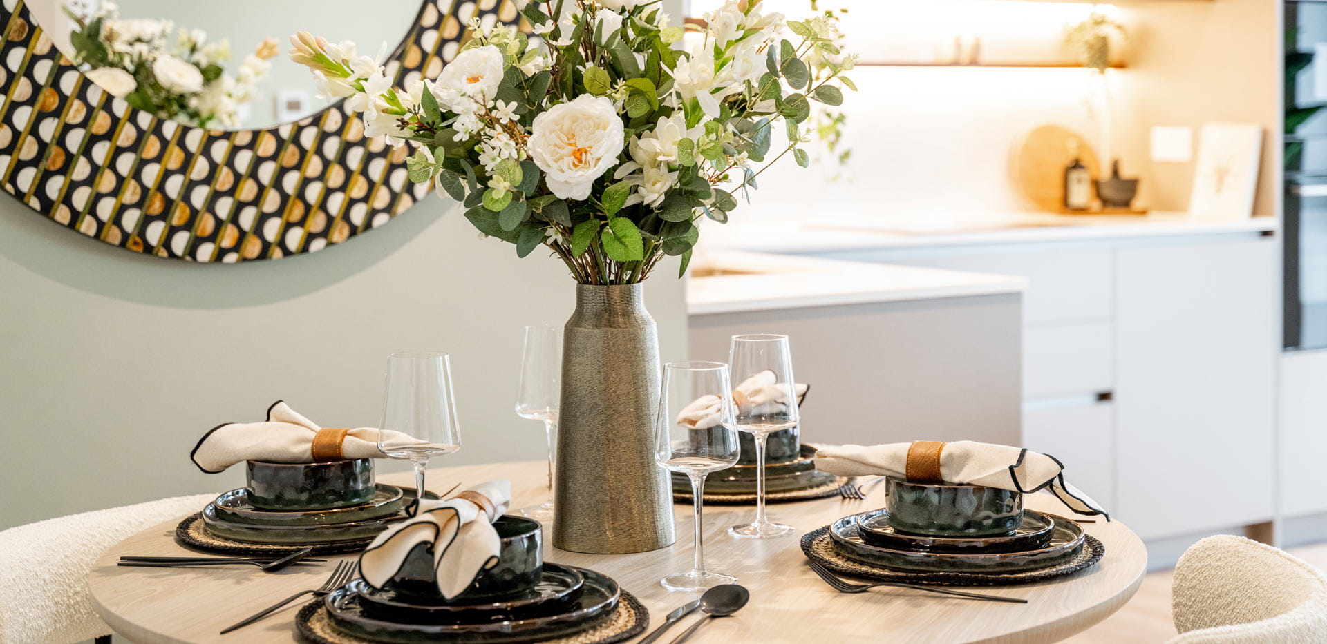 Closeup of decorated dining table with elaborate circular wall hanging mirror behind.