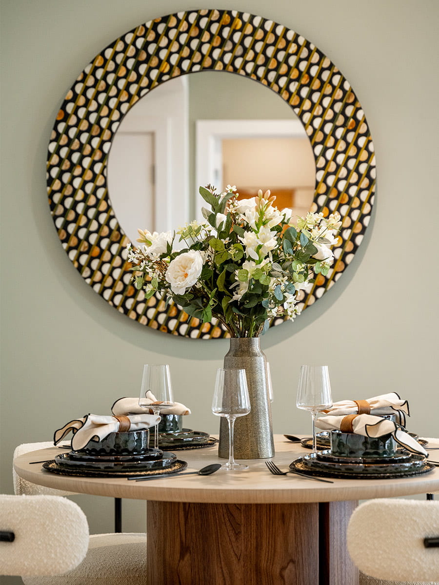 Closeup of decorated dining table with elaborate circular wall hanging mirror behind.
