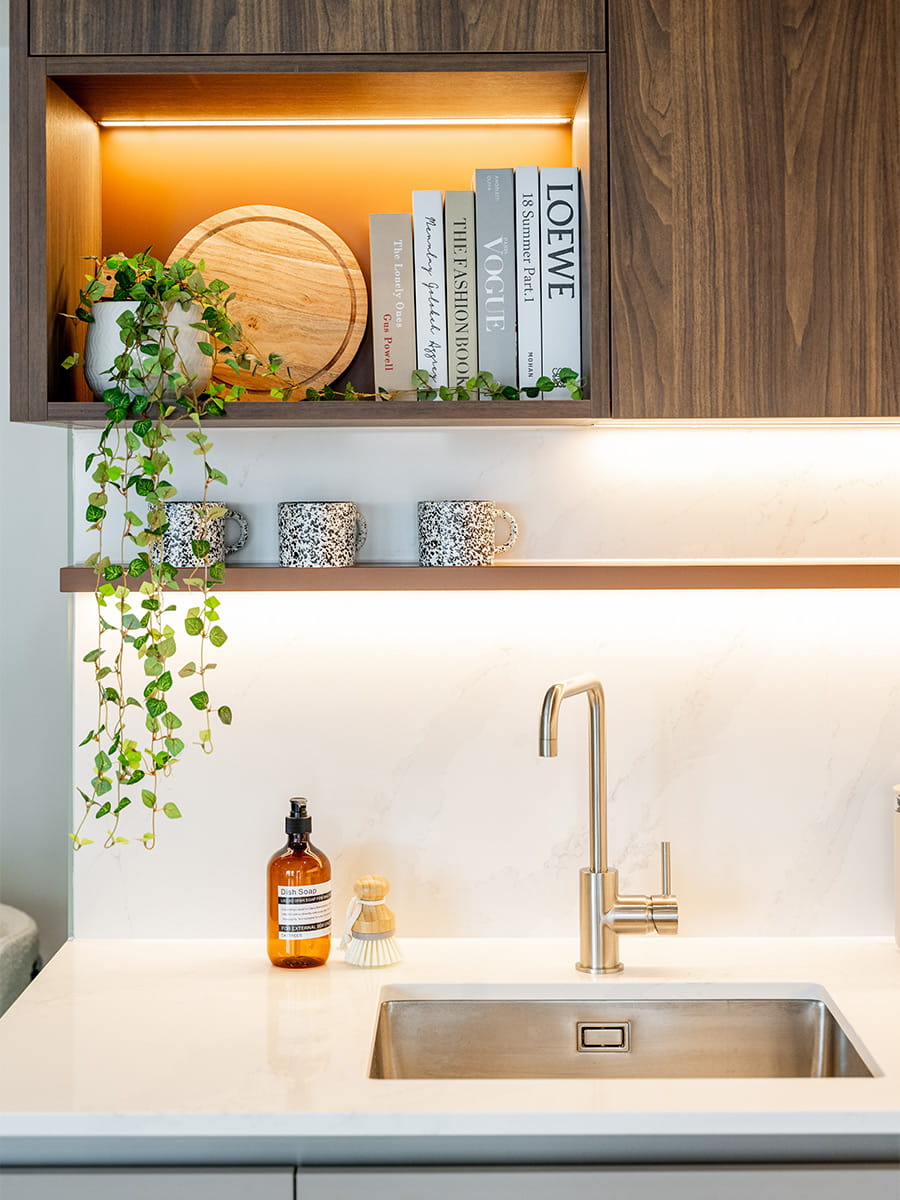 View of kitchen with modern appliances, white counters, chrome taps, strip lighting, overhead cupboards.